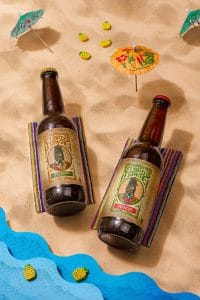Botellas de cerveza en la playa, rodeadas de sombrillas y sillas de playa, evocando un ambiente relajante y veraniego.